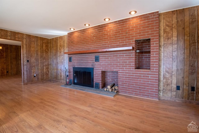 unfurnished living room featuring a fireplace, light wood-type flooring, and wooden walls