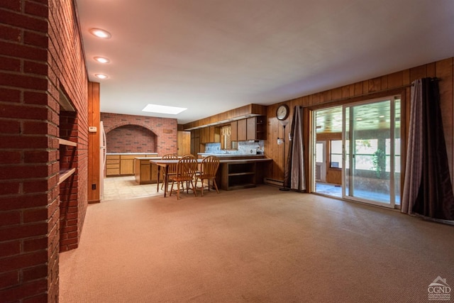 unfurnished living room featuring brick wall, baseboard heating, light carpet, and wooden walls