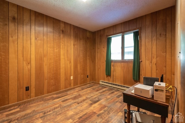 unfurnished room featuring wood walls, wood-type flooring, a textured ceiling, and a baseboard heating unit