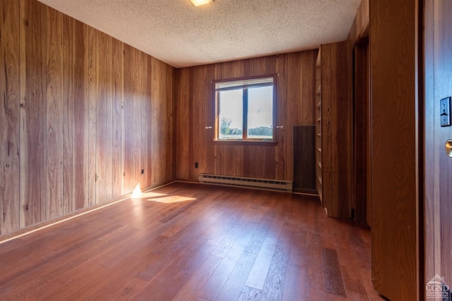 spare room with a textured ceiling, a baseboard radiator, dark hardwood / wood-style floors, and wooden walls