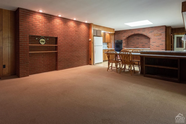 interior space featuring a breakfast bar, wooden walls, white fridge, light colored carpet, and brick wall