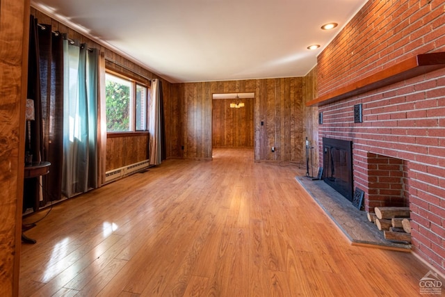 unfurnished living room with a brick fireplace, wood walls, baseboard heating, and light hardwood / wood-style flooring