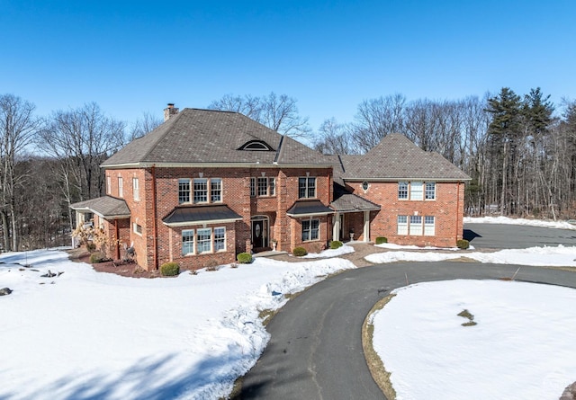 colonial-style house with a chimney, aphalt driveway, and brick siding