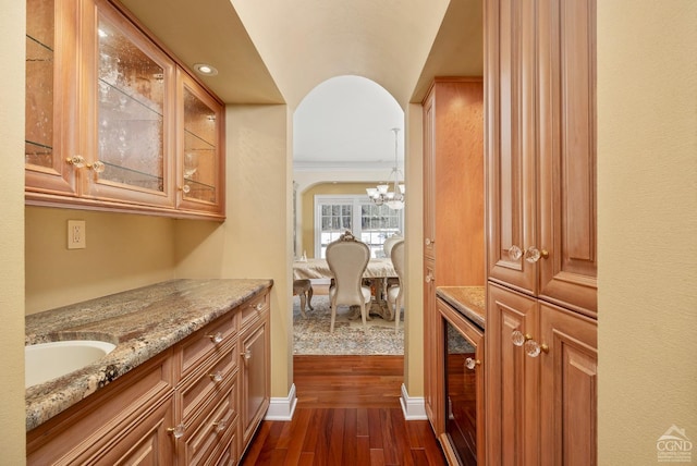 corridor with beverage cooler, arched walkways, dark wood-style floors, an inviting chandelier, and a sink