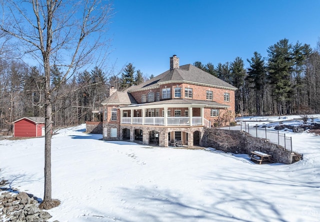 snow covered back of property with a garage, stone siding, a chimney, and an outbuilding