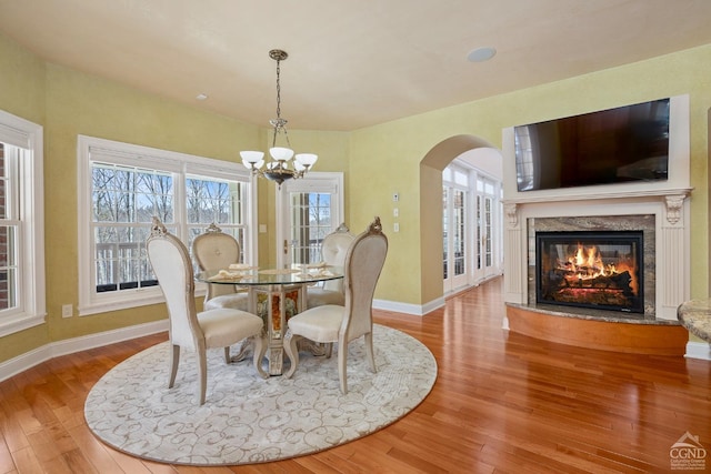 dining area with a chandelier, arched walkways, a fireplace, wood finished floors, and baseboards