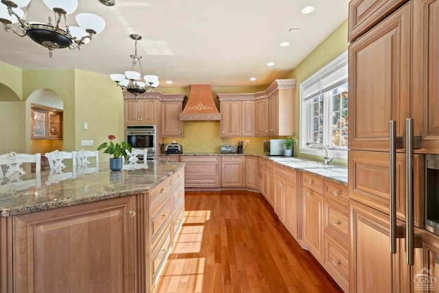 kitchen featuring light wood finished floors, custom exhaust hood, an inviting chandelier, stainless steel double oven, and a sink