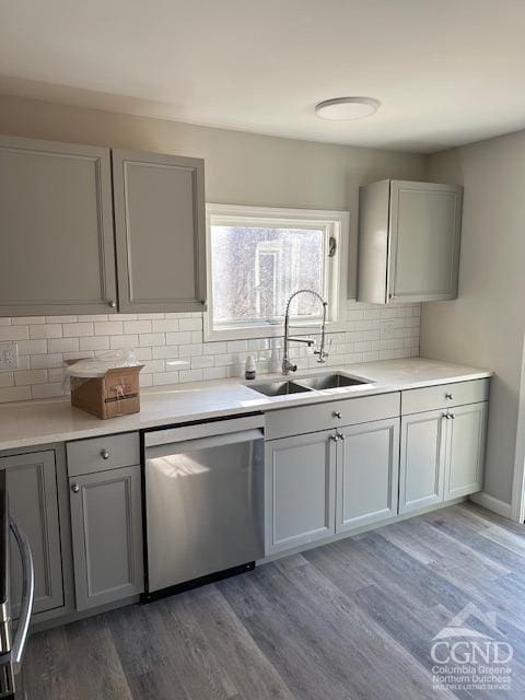 kitchen with sink, tasteful backsplash, dark hardwood / wood-style flooring, stainless steel dishwasher, and gray cabinets