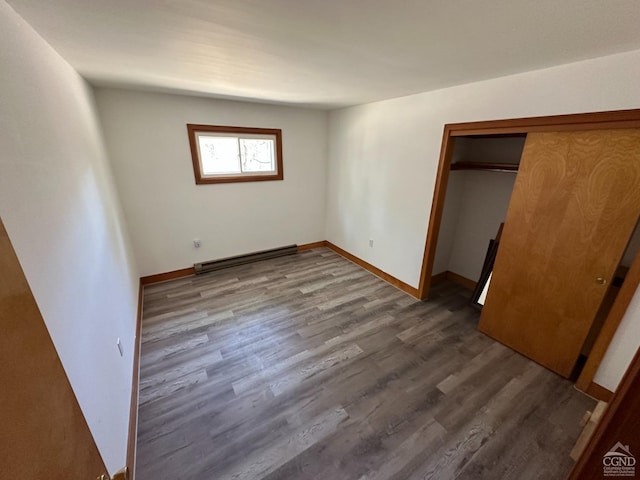 unfurnished bedroom with baseboards, a baseboard heating unit, wood finished floors, and a closet