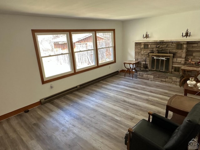 living room featuring baseboard heating, baseboards, a fireplace, and wood finished floors