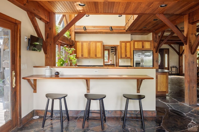 kitchen featuring kitchen peninsula, stainless steel fridge, a kitchen breakfast bar, wood ceiling, and beamed ceiling