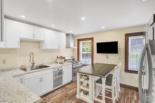 kitchen with light hardwood / wood-style floors, appliances with stainless steel finishes, white cabinetry, wall chimney range hood, and sink