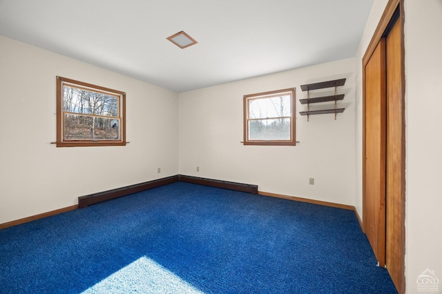 unfurnished bedroom featuring multiple windows, dark carpet, and a baseboard heating unit