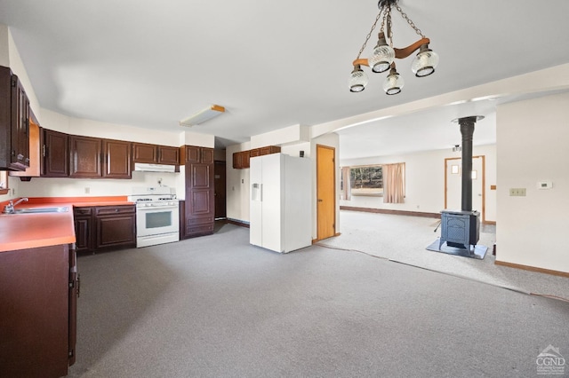 kitchen featuring a wood stove, sink, carpet floors, decorative light fixtures, and white appliances