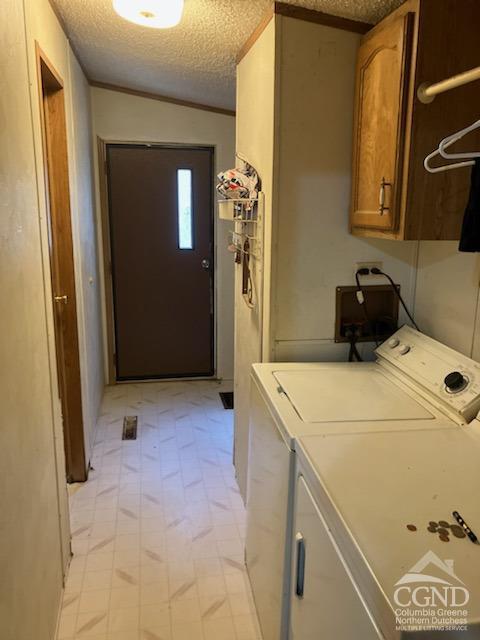 clothes washing area with cabinets, a textured ceiling, washer and clothes dryer, and ornamental molding