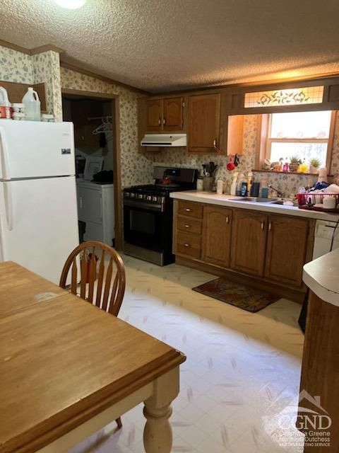 kitchen featuring black gas range, washing machine and dryer, white fridge, vaulted ceiling, and a textured ceiling