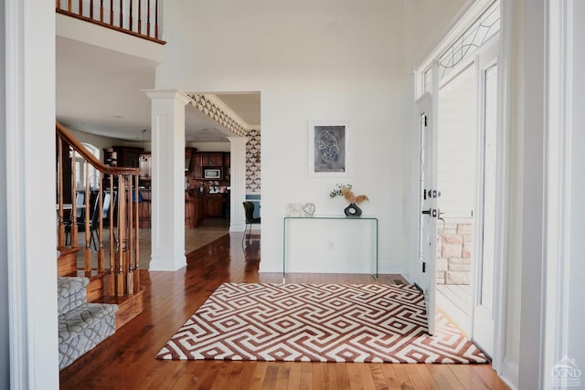 entryway featuring stairway, decorative columns, a high ceiling, and hardwood / wood-style flooring
