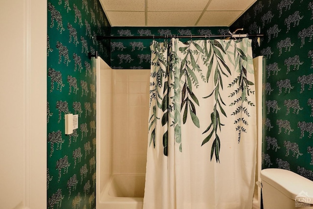 bathroom with shower / tub combo with curtain, a drop ceiling, toilet, and wallpapered walls