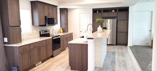 kitchen with a center island with sink, sink, appliances with stainless steel finishes, dark brown cabinets, and light hardwood / wood-style floors