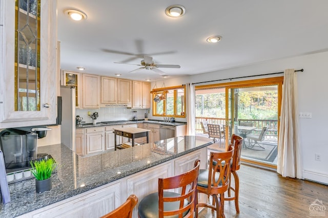 kitchen featuring ceiling fan, stainless steel appliances, wood-type flooring, decorative backsplash, and light brown cabinetry