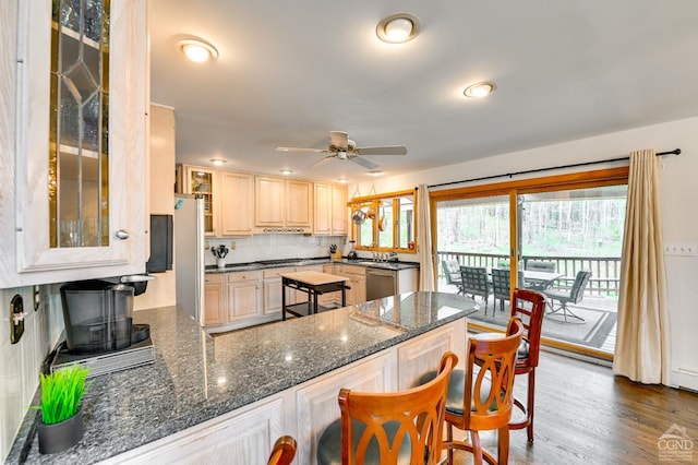 kitchen with decorative backsplash, stainless steel dishwasher, ceiling fan, dark wood-type flooring, and dark stone countertops