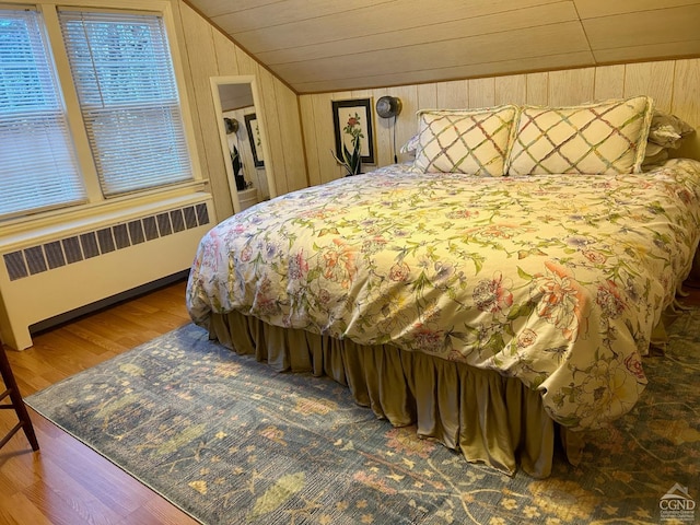 bedroom with wooden walls, lofted ceiling, hardwood / wood-style flooring, and radiator