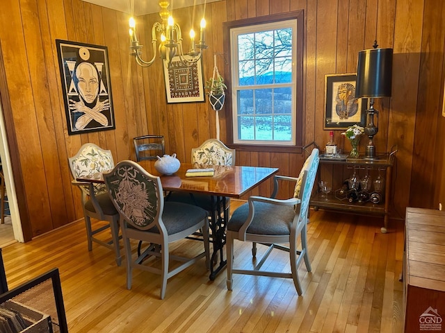 dining space featuring wood walls, light hardwood / wood-style floors, and a notable chandelier