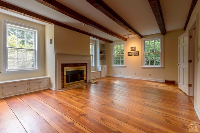 unfurnished living room featuring beam ceiling, light hardwood / wood-style flooring, and a healthy amount of sunlight