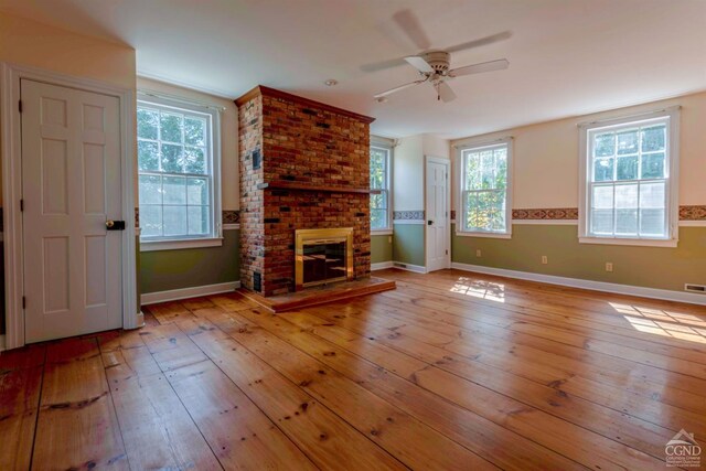 unfurnished living room featuring a fireplace, ceiling fan, plenty of natural light, and light wood-type flooring