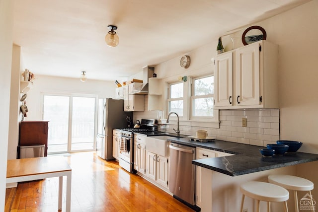 kitchen with wall chimney range hood, dark countertops, tasteful backsplash, a breakfast bar, and stainless steel appliances