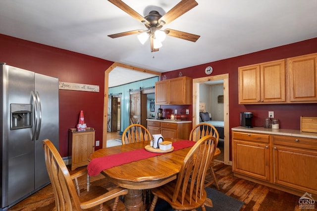 dining area featuring a barn door, dark wood-type flooring, and ceiling fan