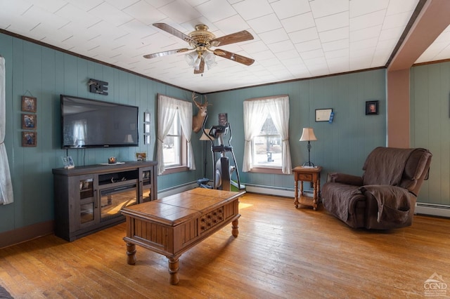 living area featuring a baseboard radiator, light wood-style floors, ornamental molding, and a ceiling fan