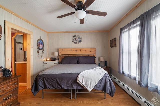 bedroom featuring a baseboard heating unit, multiple windows, wood finished floors, and ceiling fan