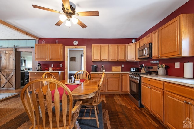 kitchen with dark wood-style flooring, ceiling fan, light countertops, appliances with stainless steel finishes, and a barn door