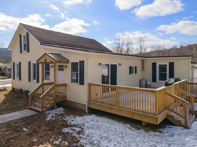 snow covered rear of property with roof with shingles