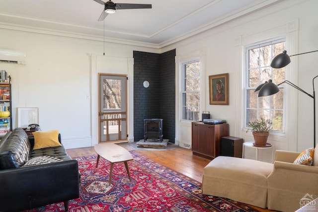 living room featuring a wood stove, ceiling fan, a wall mounted AC, crown molding, and hardwood / wood-style floors