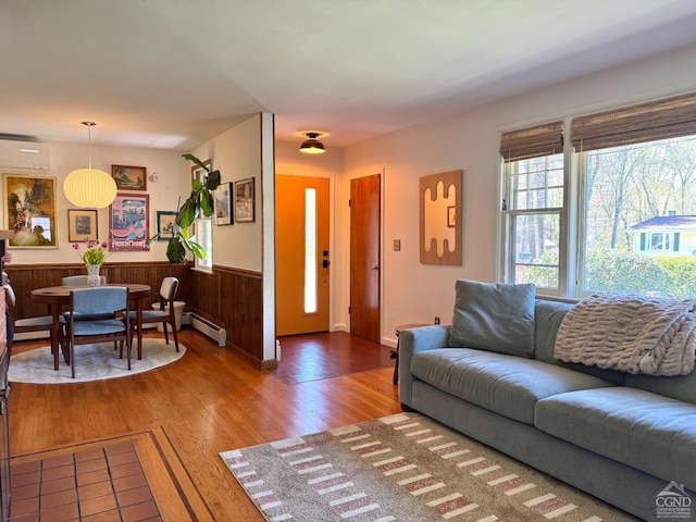 living room featuring wood finished floors, a wall unit AC, a wainscoted wall, wood walls, and baseboard heating