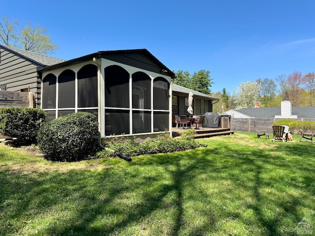 rear view of property with a yard, a deck, a sunroom, and fence