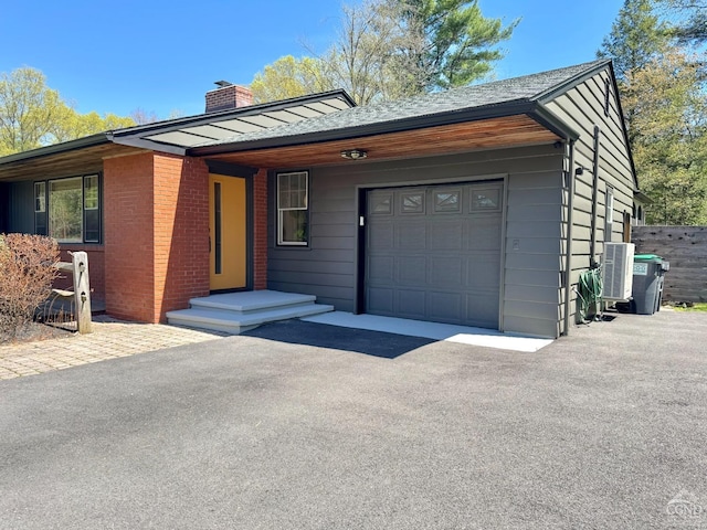 view of front of house with a garage, cooling unit, fence, a chimney, and driveway