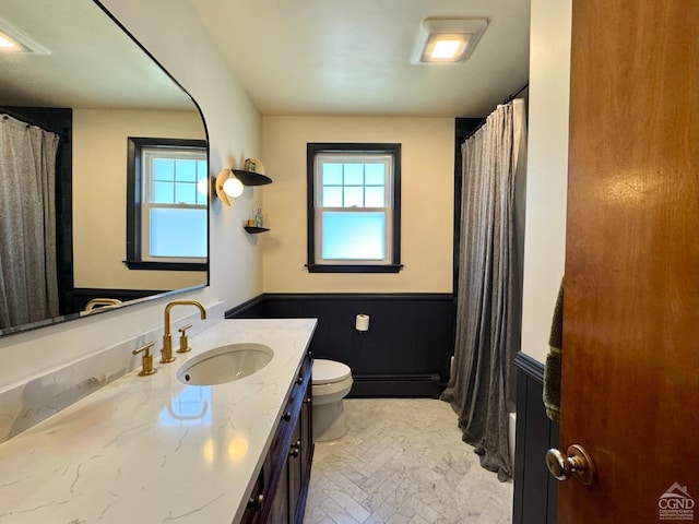 bathroom with a wealth of natural light, wainscoting, toilet, and a baseboard radiator