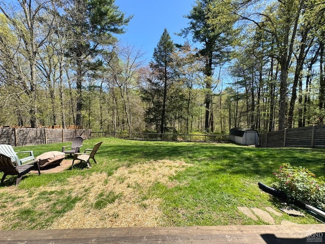 view of yard featuring a fire pit, an outdoor structure, a fenced backyard, and a shed