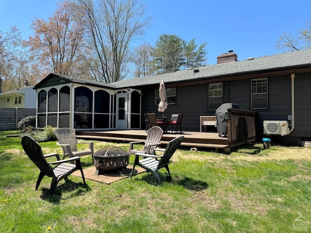 rear view of house with a yard, a sunroom, a wooden deck, and a fire pit