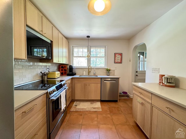 kitchen with a sink, decorative backsplash, light brown cabinetry, arched walkways, and appliances with stainless steel finishes