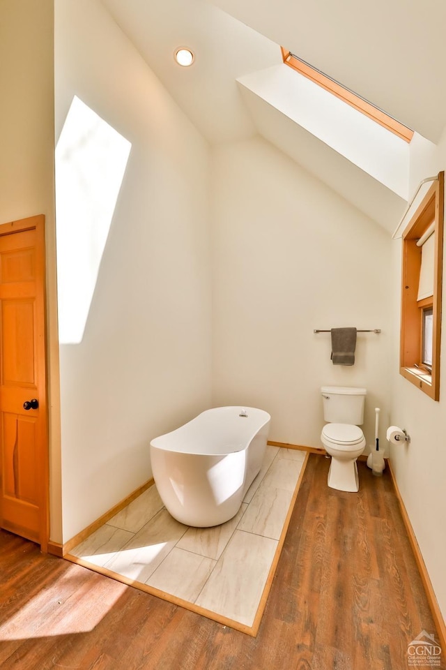 bathroom with toilet, hardwood / wood-style flooring, lofted ceiling with skylight, and a bathing tub