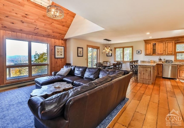 living room with wooden walls, a notable chandelier, lofted ceiling, and light wood-type flooring