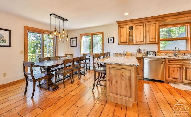 kitchen featuring a kitchen bar, light wood-type flooring, stainless steel dishwasher, sink, and decorative light fixtures