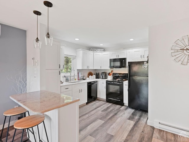 kitchen with white cabinetry, sink, a kitchen bar, black appliances, and light wood-type flooring