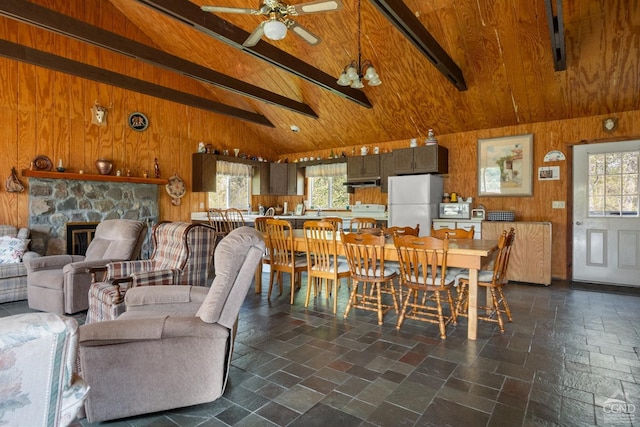 dining room with beamed ceiling, high vaulted ceiling, a stone fireplace, and ceiling fan