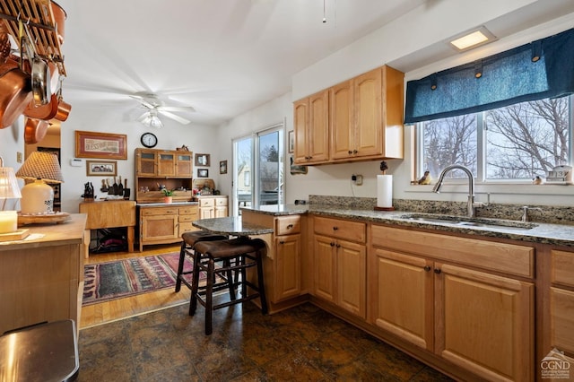 kitchen with stone counters, a peninsula, ceiling fan, and a sink