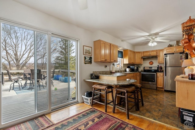 kitchen featuring ceiling fan, dark wood finished floors, a peninsula, appliances with stainless steel finishes, and under cabinet range hood